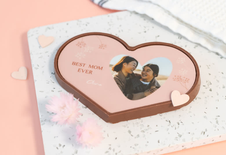 Heart-shaped chocolate with customisable photo and "Best Mom Ever" text on a pink background. Decorated with small hearts.