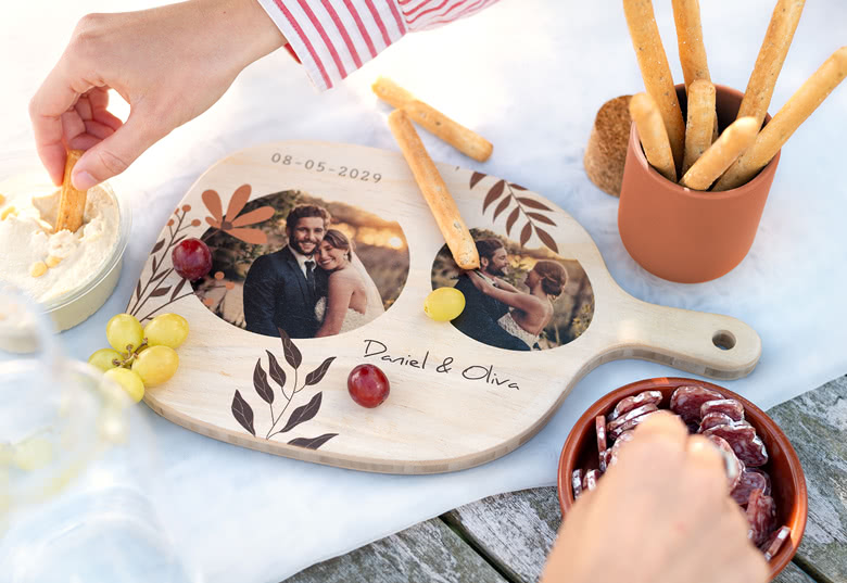 Personalised wooden cutting board with two circular photo prints, date, and names "Daniel & Olivia" in black text on a light wood background.