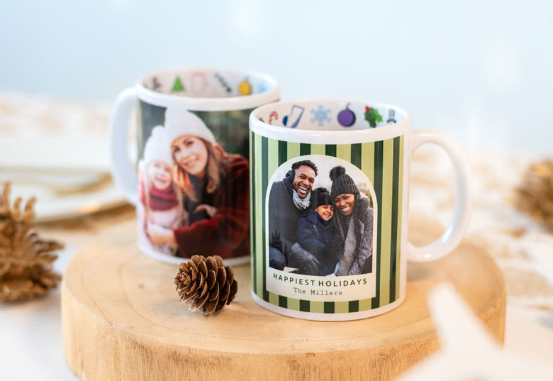 Personalised Christmas mugs featuring family photos, festive icons, and a "Happiest Holidays" message on a green striped background.
