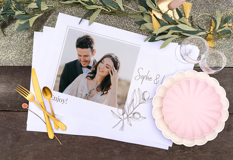 Set van gepersonaliseerde placemats met een foto van een stel, namen "Sophie & I", en bloemillustraties. Witte achtergrond.