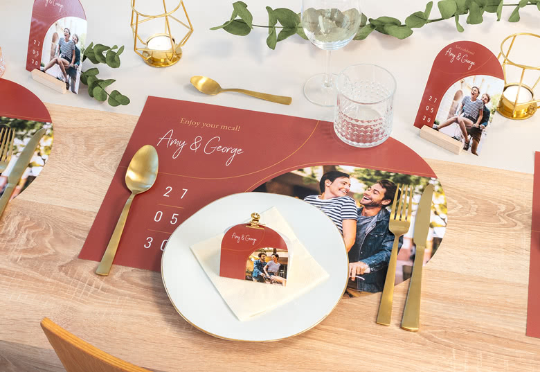 Gepersonaliseerde placemats met een kastanjebruine achtergrond, aanpasbaar met namen en foto’s, gerangschikt op een eettafel met gouden bestek.
