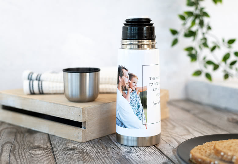 Gepersonaliseerde thermosfles met een eigen foto en tekst, met een zilveren basis, zwarte dop en een witte body die de afbeelding en boodschap weergeeft.